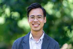 Paul Tran Hoang stands before a green blurred background of trees.
