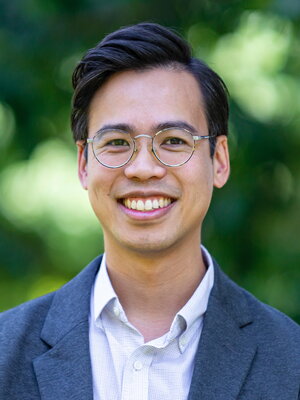 Paul Tran Hoang stands before a green blurred background of trees.